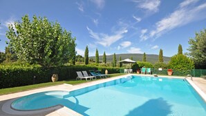 Une piscine avec des chaises longues, une pergola et une vue sur les collines.