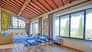 Un salon spacieux avec une grande fenêtre, un canapé, un fauteuil bleu et un tapis à motifs.