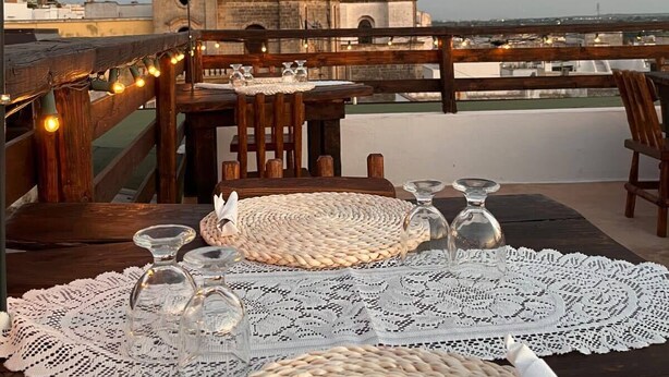 A rooftop terrace with a table set for dining, overlooking a historic tower and cityscape. - A Locanda Tù Marchese (Matino)