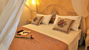 A bed with a canopy, two pillows with floral designs, a bedside table with a lamp, and a book and glasses on the bed. - A Locanda Tù Marchese (Matino)