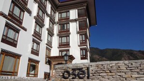 A traditional building with a stone wall in front, a sign reading "osel", and a mountainous backdrop. - Hotel Osel (Thimphu)