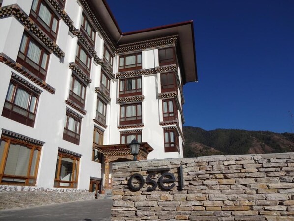 A traditional building with a stone wall in front, a sign reading "osel", and a mountainous backdrop. - Hotel Osel (Thimphu)