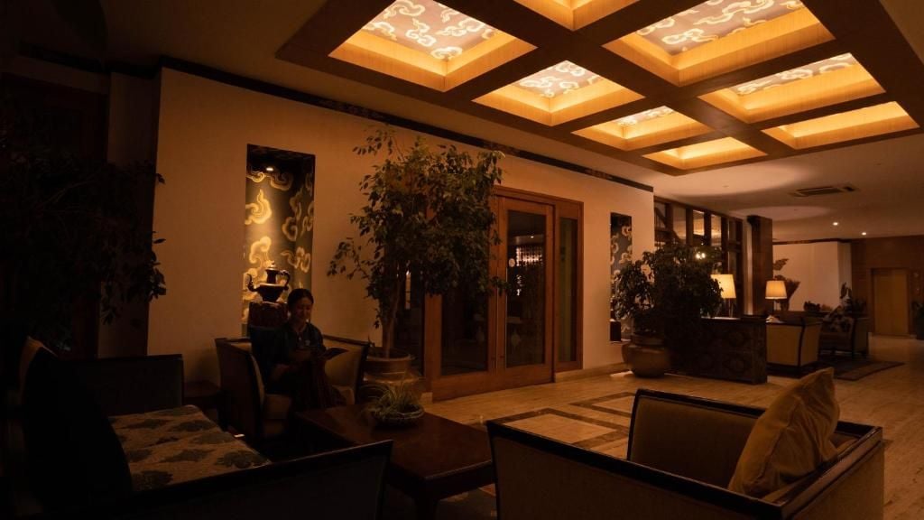A dimly lit lounge area with a large plant, a sofa, and a table.