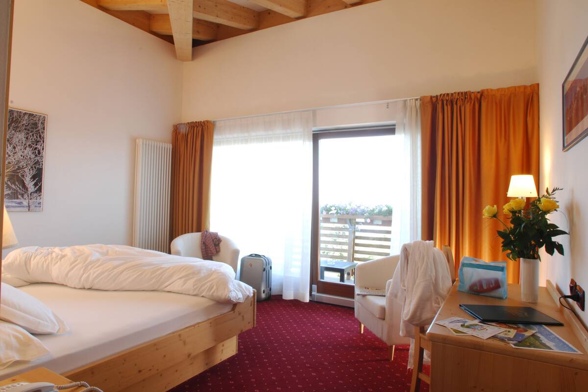 Une chambre d’hôtel avec un lit, un bureau avec une lampe, une chaise, une valise et une vue sur l’extérieur.