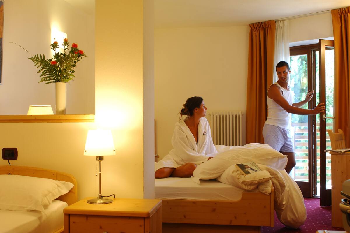 Une chambre d’hôtel avec un lit, une lampe de chevet, une table de chevet en bois et une fenêtre avec des rideaux.