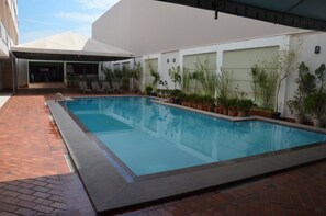 A rectangular pool with a tiled edge, surrounded by potted plants and a covered seating area.
