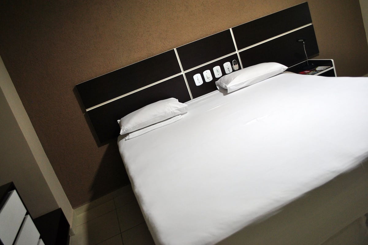 A hotel room with a large bed, a nightstand, and a wall clock.