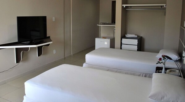 Quarto de hotel com duas camas, televisão, guarda-roupa e uma pequena mesa de cabeceira com um vaso de flores.