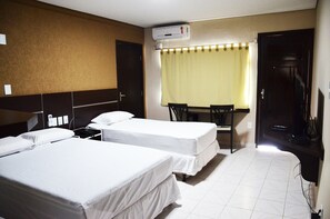 A hotel room with two beds, a desk, and a chair. There is an air conditioning unit on the wall and a door to the right.