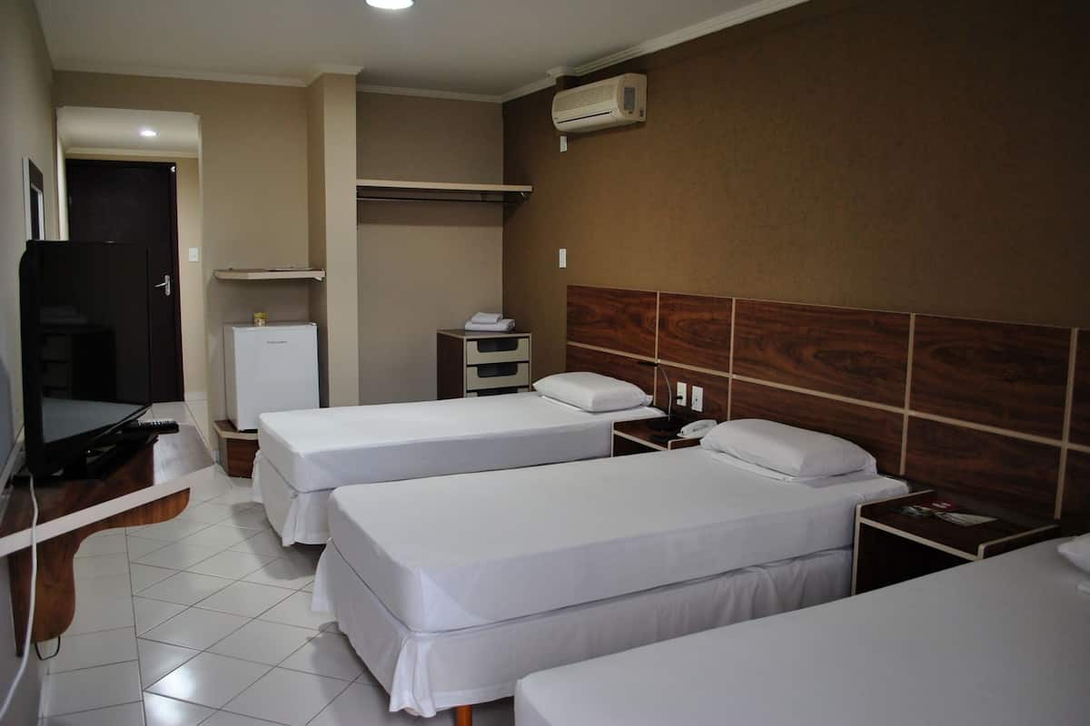 A hotel room with two single beds, a TV, a refrigerator, a bedside table, and a wooden headboard.