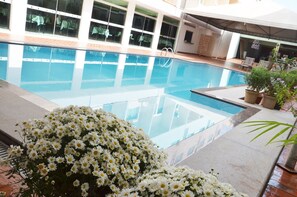 Piscina interior com água cristalina, rodeada por plantas em vasos e chão revestido de azulejos.