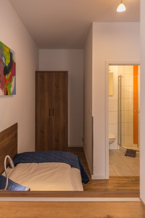 Un dormitorio con cama, armario de madera y baño con ducha e inodoro.