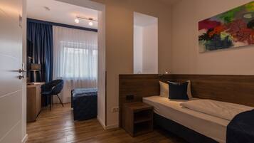 Ein modernes Hotelzimmer mit Holzboden, einem Bett mit weißen Leinentüchern, einem Schreibtisch mit Stuhl und einem Bild an der Wand.
