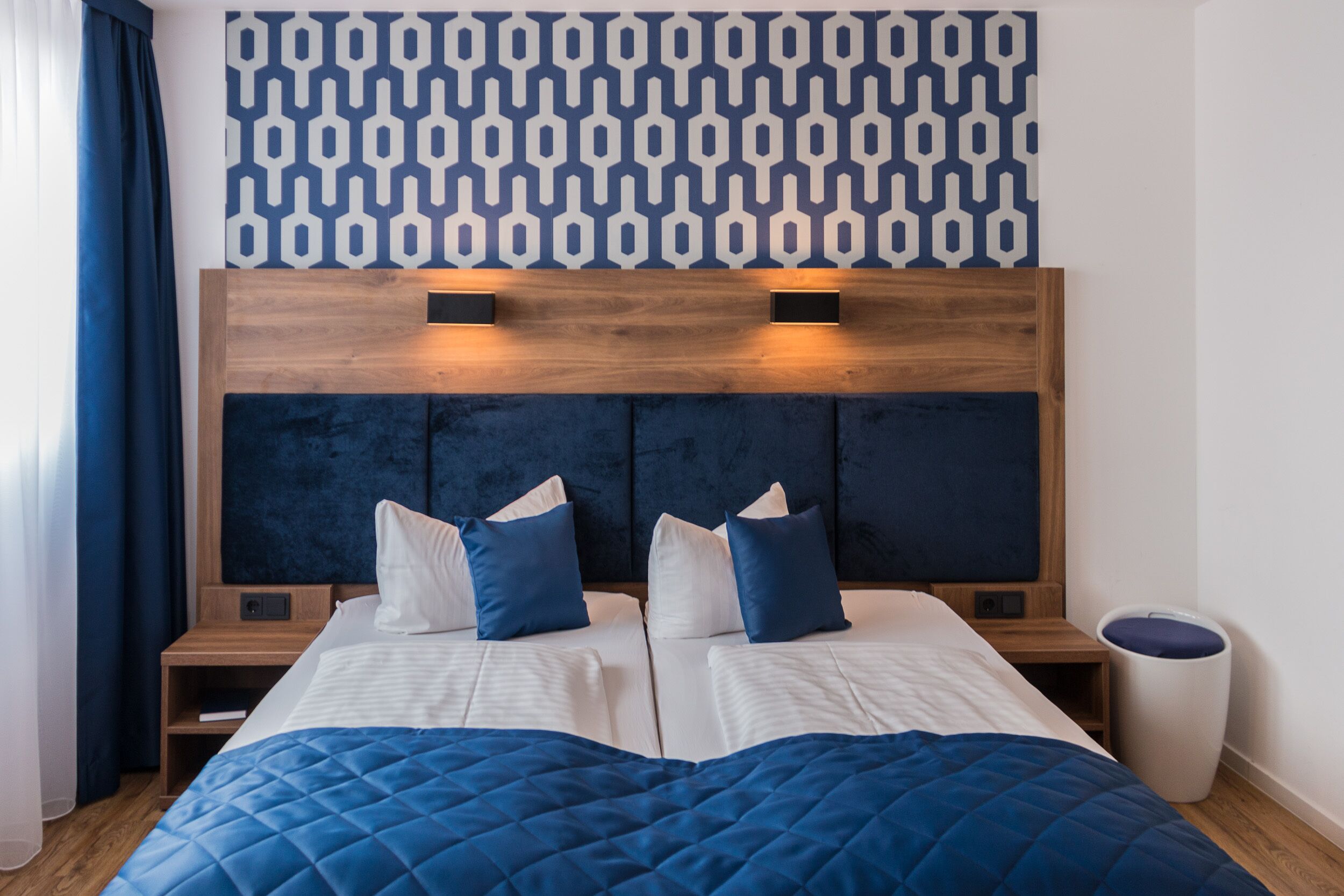Una habitación de hotel con una cama grande, dos mesitas de noche, un cabecero de madera y un papel tapiz estampado.