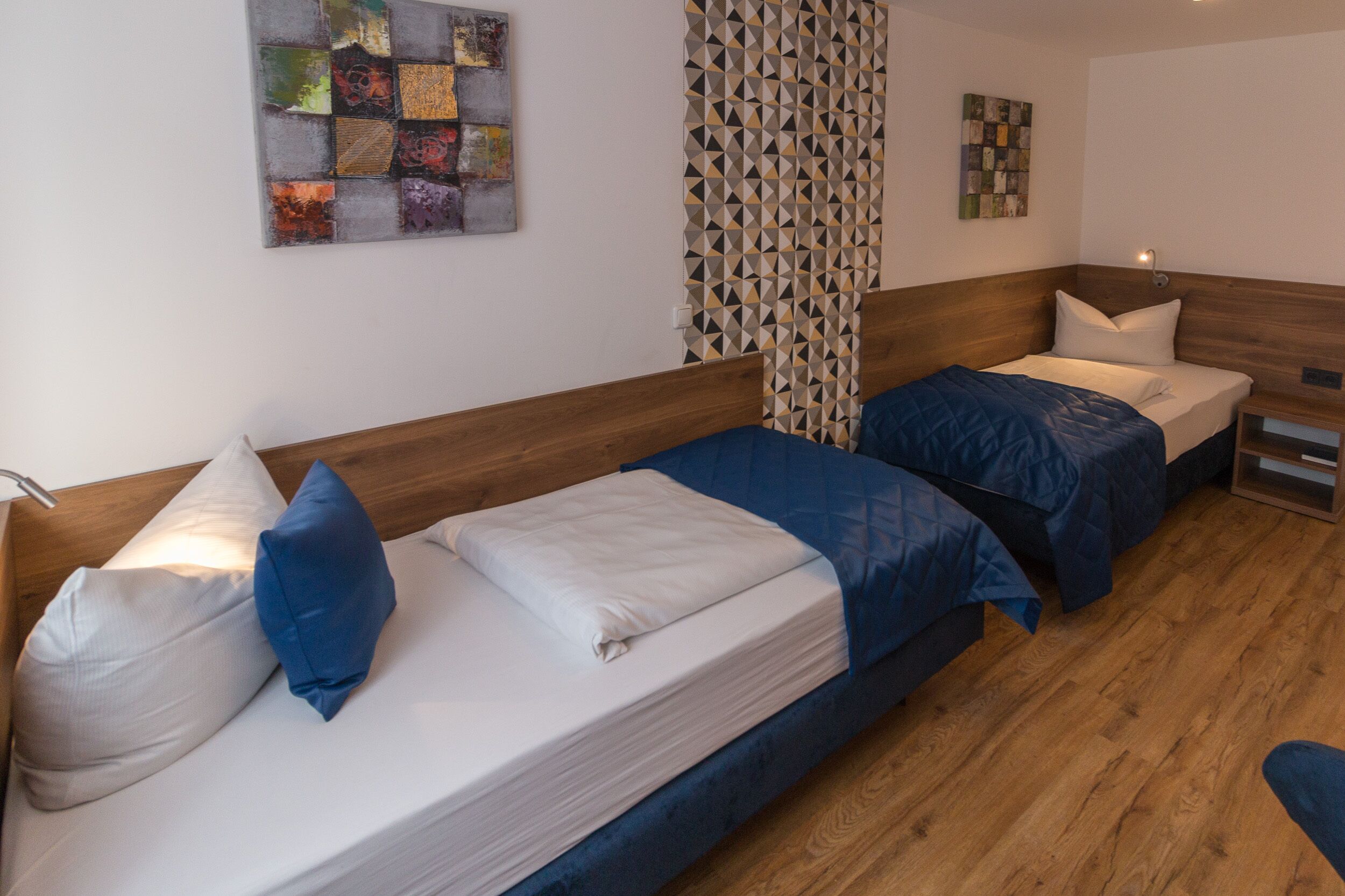 A room with two beds, wooden headboards, a patterned curtain, and a wall-mounted artwork.