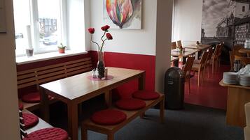 A restaurant with wooden tables and red cushioned benches, a large window with a view, and a colorful abstract painting on the wall.