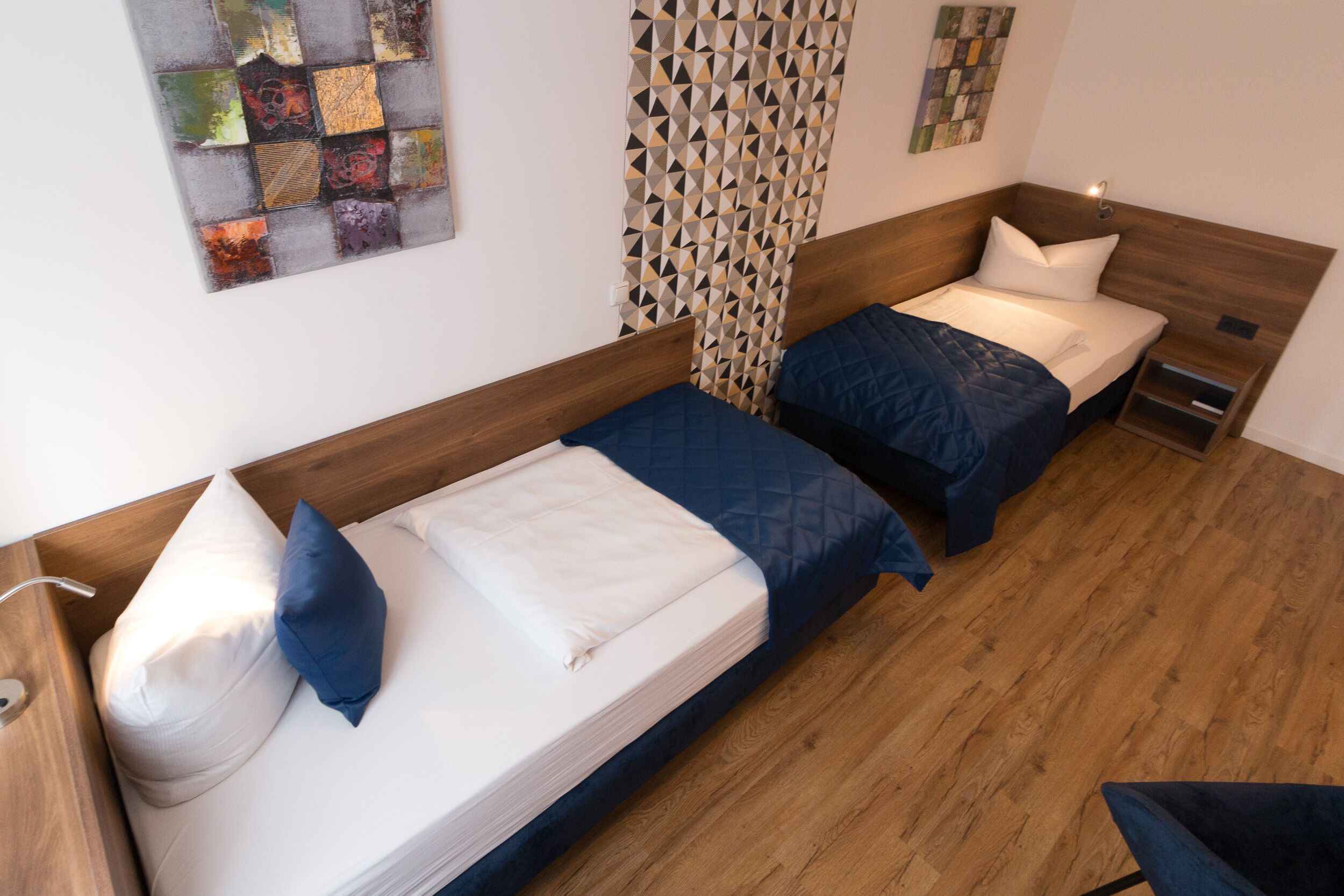 A room with two single beds, wooden headboards, a small bedside table, and a wall-mounted artwork.