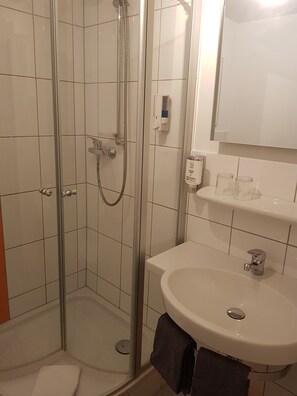 Un baño con cabina de ducha de vidrio, un lavamanos blanco con espejo superior y un inodoro.