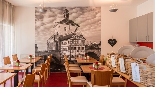 Un restaurante con mesas y sillas de madera, un mural de un paisaje urbano europeo y un piso alfombrado en rojo.