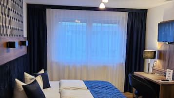 Une chambre d’hôtel avec un lit, un bureau, une chaise, une télévision et une fenêtre avec des rideaux.