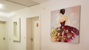 Un pasillo con una silla roja, una lámpara y un cuadro de una mujer con un vestido colorido en la pared.