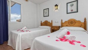 A hotel room with two single beds, a window with a view, a wall-mounted lamp, and a framed picture. - Embajador Apartamentos (Fuengirola)