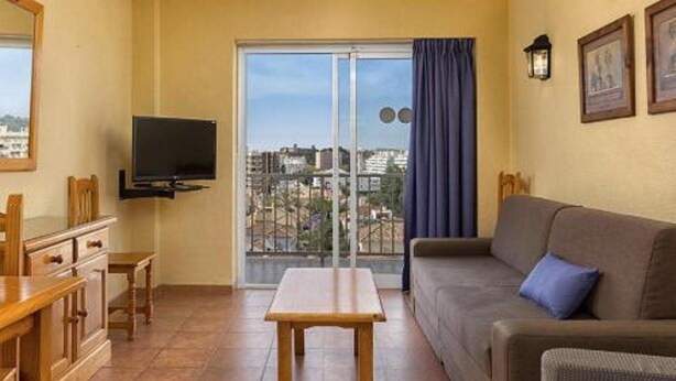 A balcony with a view of buildings, a sofa, a TV, and a table. - Embajador Apartamentos (Fuengirola)