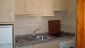 A kitchen with light wooden cabinets, a granite countertop, a stainless steel sink, and a white stove. - Embajador Apartamentos (Fuengirola)