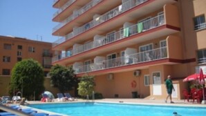 A multi-story building with balconies, a swimming pool with lounge chairs, and a person walking by. - Embajador Apartamentos (Fuengirola)