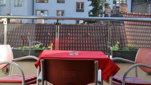 A terrace with a red table and chairs, a metal railing, and a building in the background. - Dvorak (Ceske Budejovice)