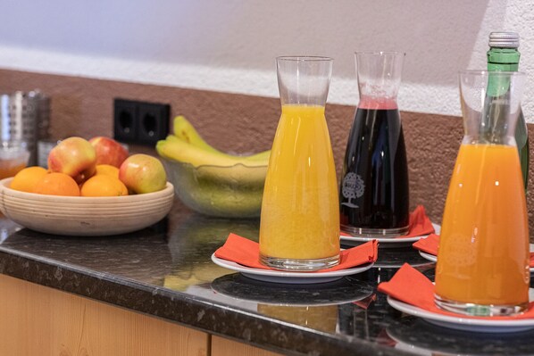 A kitchen counter with a bowl of fruit, two orange juice bottles, and a bottle of dark liquid. - Hotel Eckartauerhof (Mayrhofen)