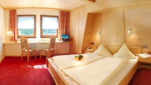 Een hotelkamer met een bed, twee stoelen, een bureau, een televisie en een raam met gordijnen.