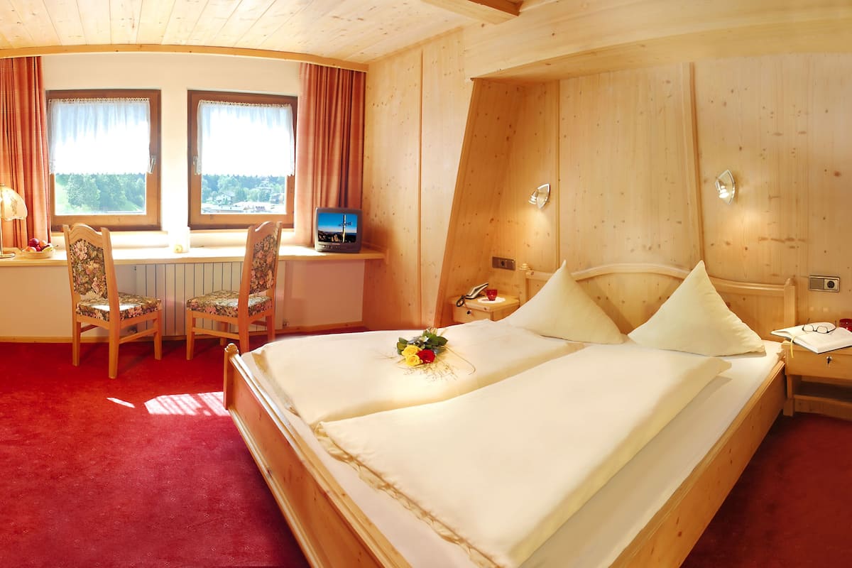 Une chambre d’hôtel avec un lit, deux chaises, un bureau, une télévision et une fenêtre avec des rideaux.