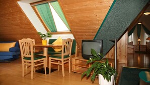Une pièce mansardée chaleureuse avec des murs en bois, une table à manger avec des chaises, un téléviseur et une plante en pot.