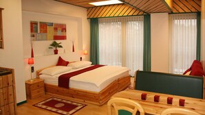 Une chambre confortable avec un lit en bois, des tables de chevet, un bureau avec des chaises et une grande fenêtre avec des rideaux.