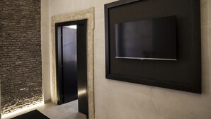 Un interior moderno con una pared de piedra, un televisor con marco negro y una puerta que conduce a otra habitación.