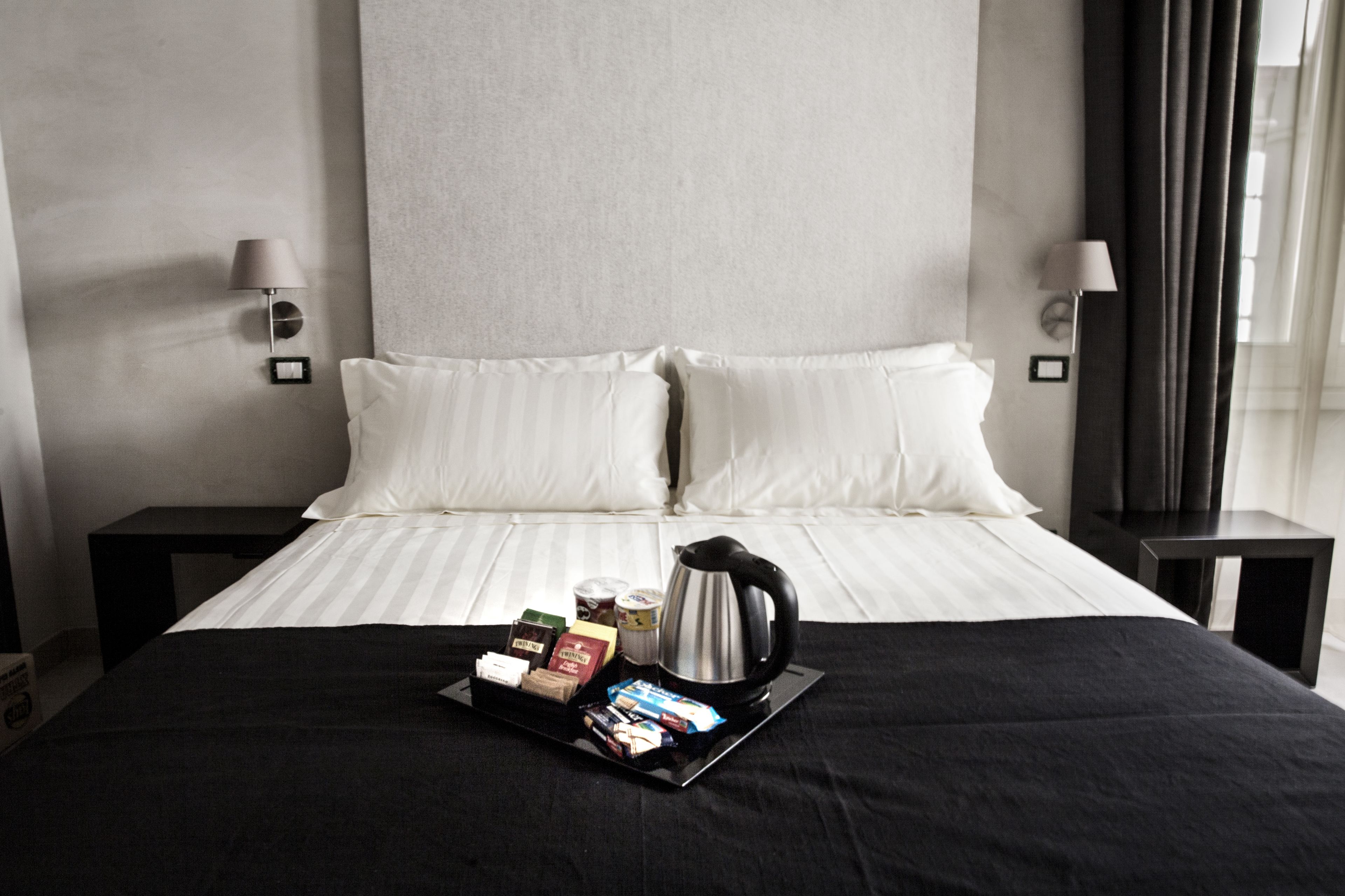 A neatly made bed with white linens, a tray of breakfast items, and a coffee maker on the bed.