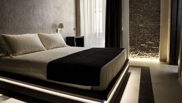 Un dormitorio moderno con una cama grande, una mesita de noche, una lámpara y una pared de piedra.