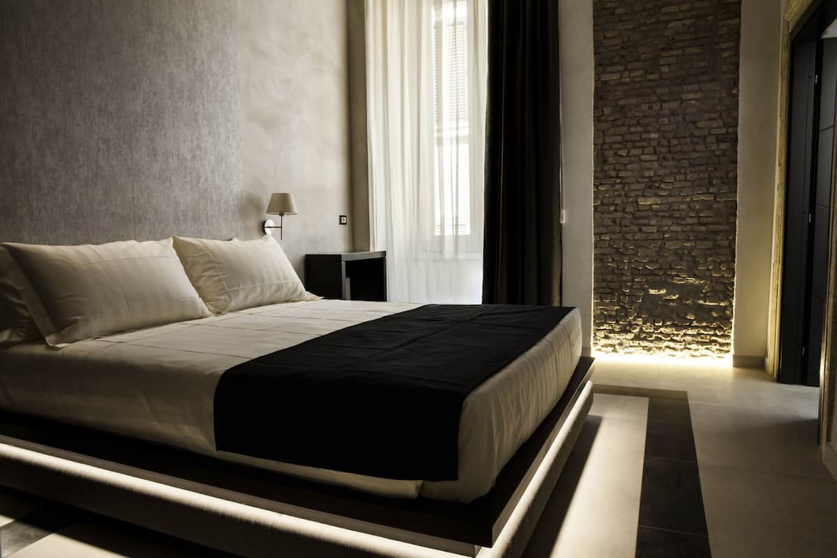 Un dormitorio moderno con una cama grande, una mesita de noche, una lámpara y una pared de piedra.