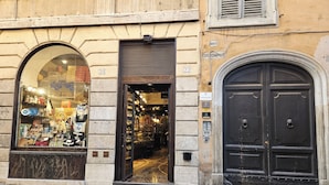 Un escaparate con un amplio ventanal de arco que muestra varios artículos, una puerta con un letrero encima y una puerta doble negra a la derecha.