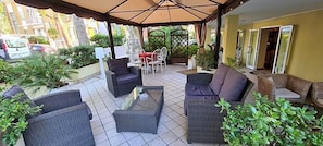 An outdoor patio with wicker furniture, a glass table, and potted plants. - Hotel Beppe (Rimini)