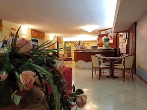 A hotel lobby with a reception desk, a dining area with chairs, and a large floral arrangement. - Hotel Beppe (Rimini)