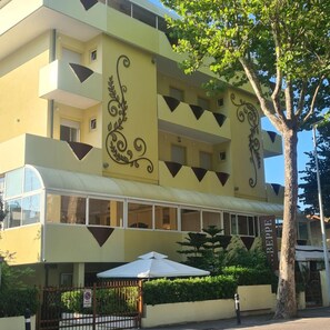 Un immeuble à plusieurs étages, doté d’une façade jaune, de motifs noirs décoratifs et d’un espace d’entrée abrité.
