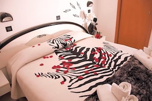 A bed with a zebra print bedspread and red rose petals, a vase with flowers, and a wooden door in the background. - Hotel Beppe (Rimini)