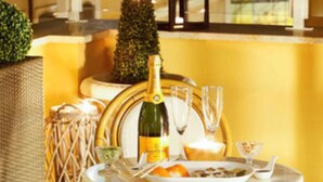 A table set with a bottle of champagne, glasses, and a plate of food, with a small tree and a lantern in the background. - Relais Monti (Rome)