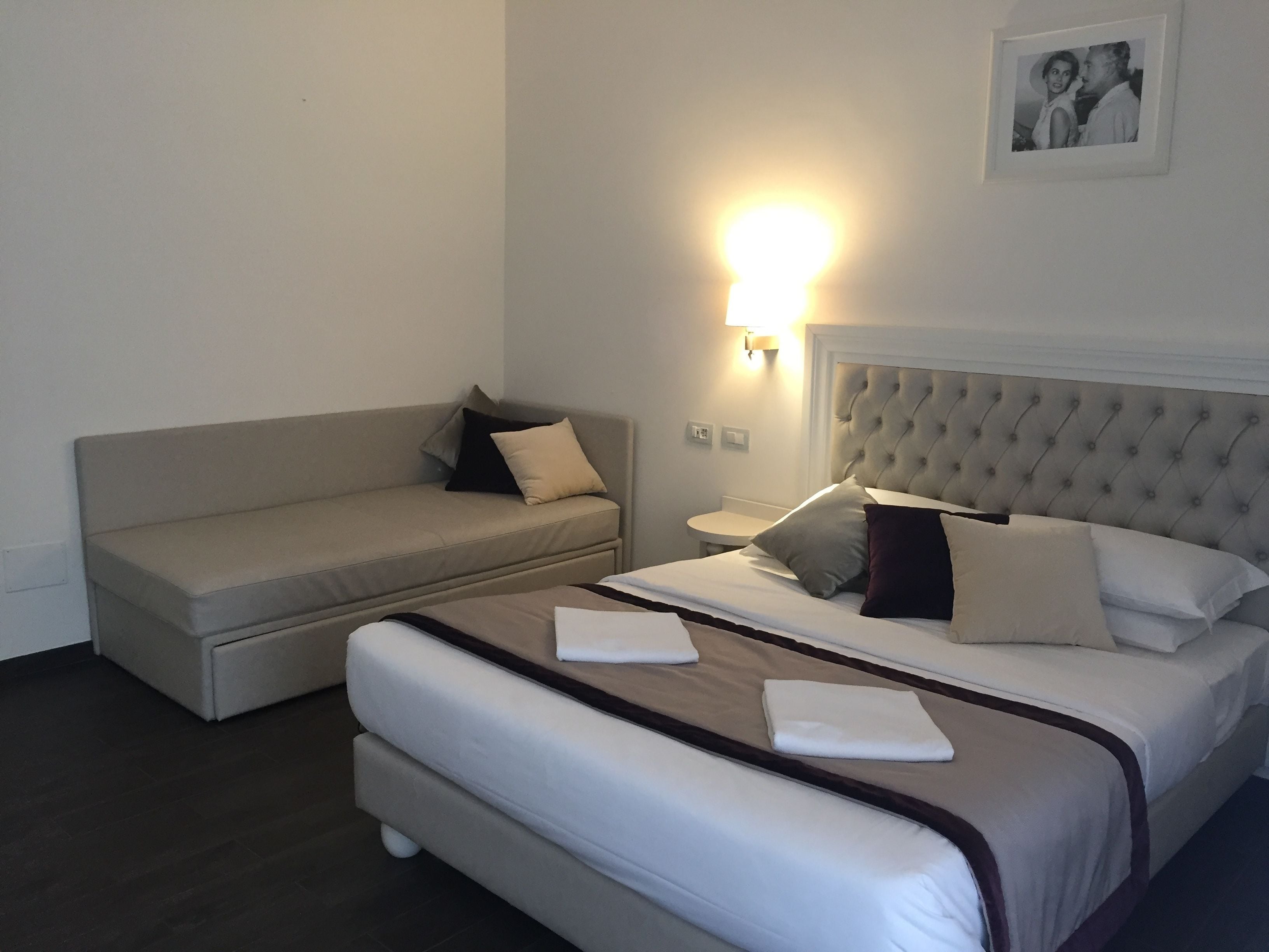 A hotel room with a bed, a sofa, and a wall-mounted lamp.