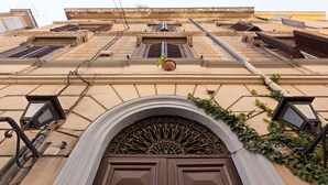 A building facade with a central arched entrance, multiple windows with shutters, and a decorative metal grille above the door. - Relais Monti (Rome)