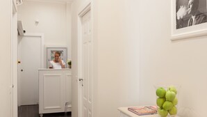 A hallway with a white door, a mirror, a small table with a map, and a green apple vase. - Relais Monti (Rome)