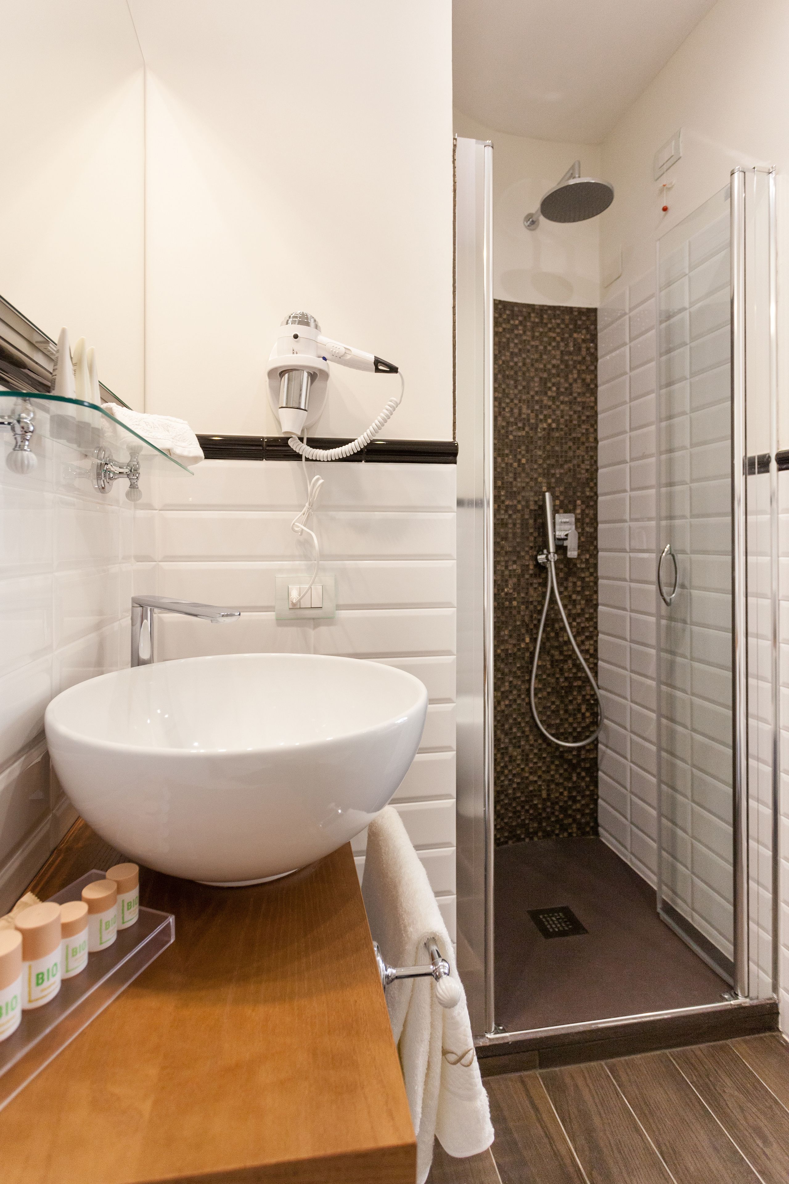 Ein modernes Badezimmer mit einem großen weißen Waschbecken, einer Duschkabine aus Glas und einem Holzlagerfläschchen.