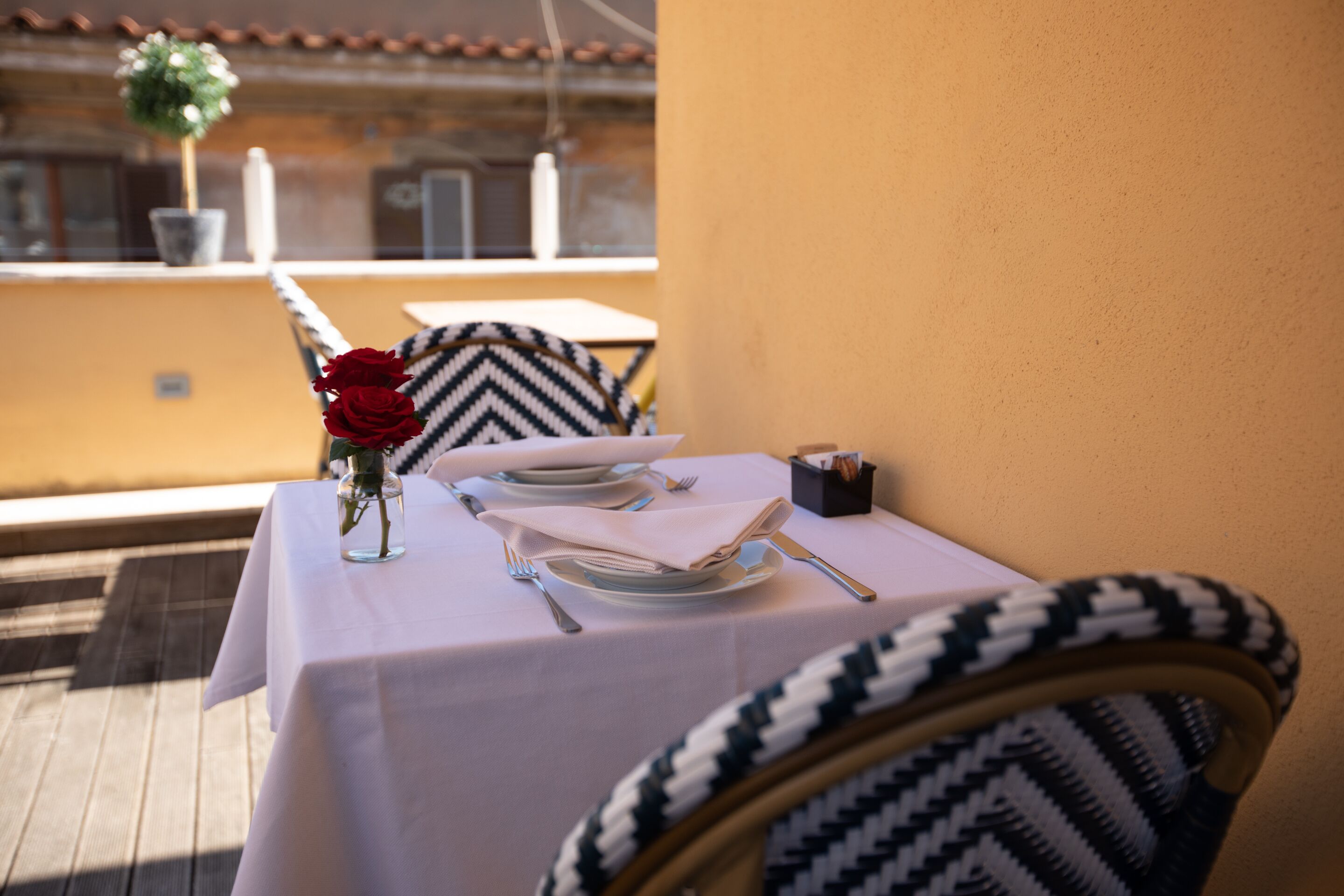 A dining table set with plates, cutlery, and a vase with red roses.